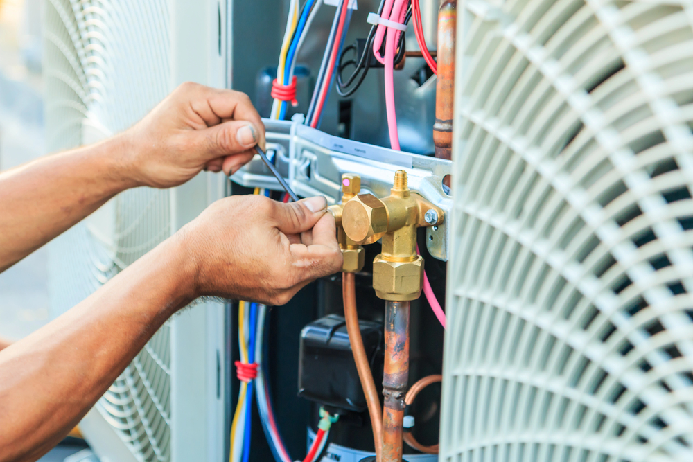 Close-up of a person repairing or maintaining the inner components of an air conditioning unit using a wrench.