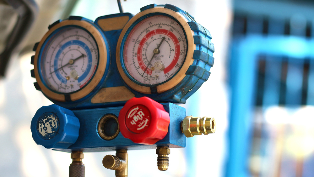 Close-up of a blue manifold gauge set with two pressure dials and red and blue valve knobs used for measuring refrigerant in HVAC systems.