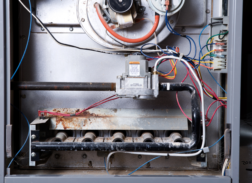 The inside of a gas furnace showing burners, wiring, metal pipes, and an igniter component mounted on a metal panel.